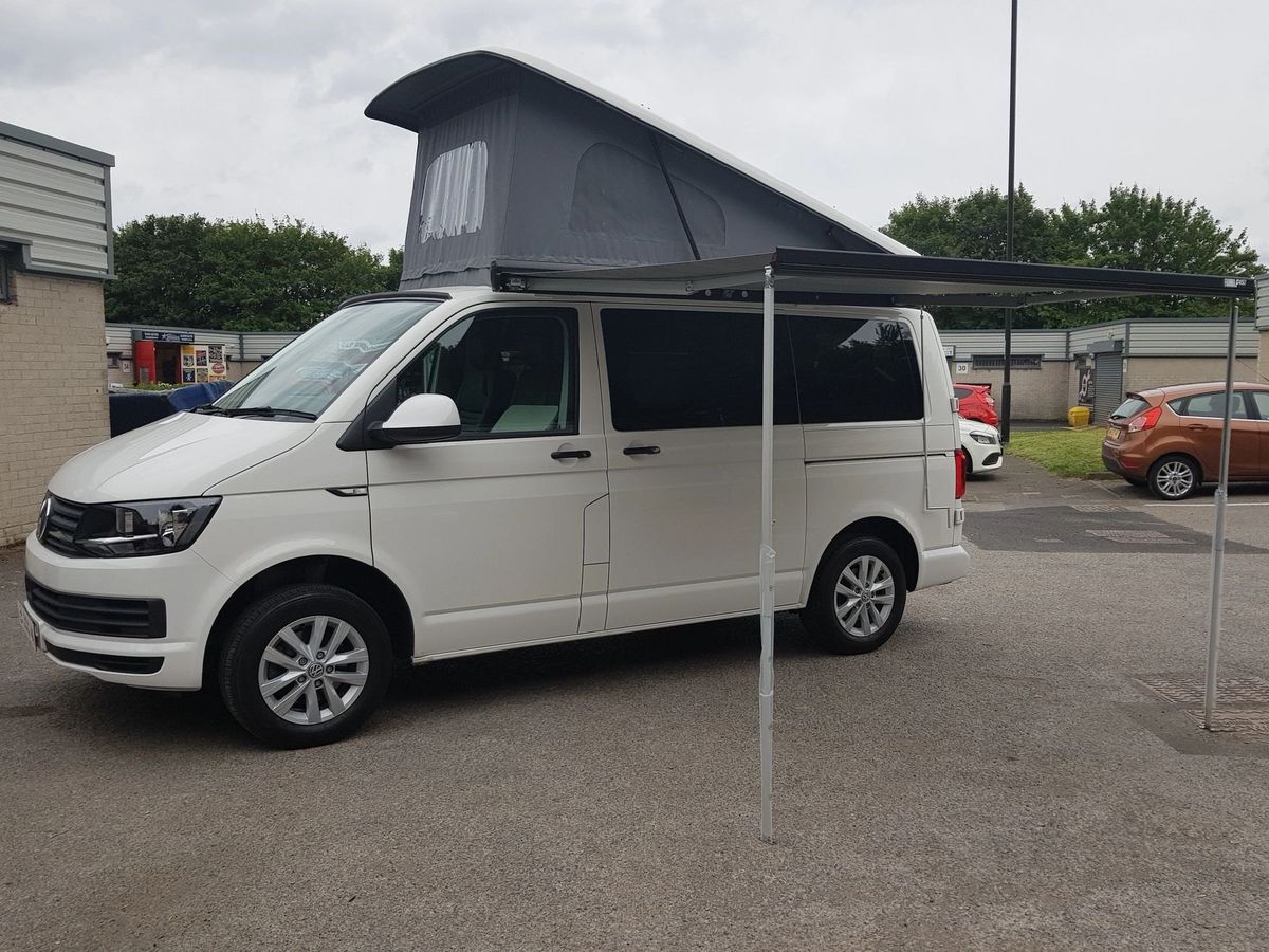White VW T6 camper with the roof raised and a wind-out awning