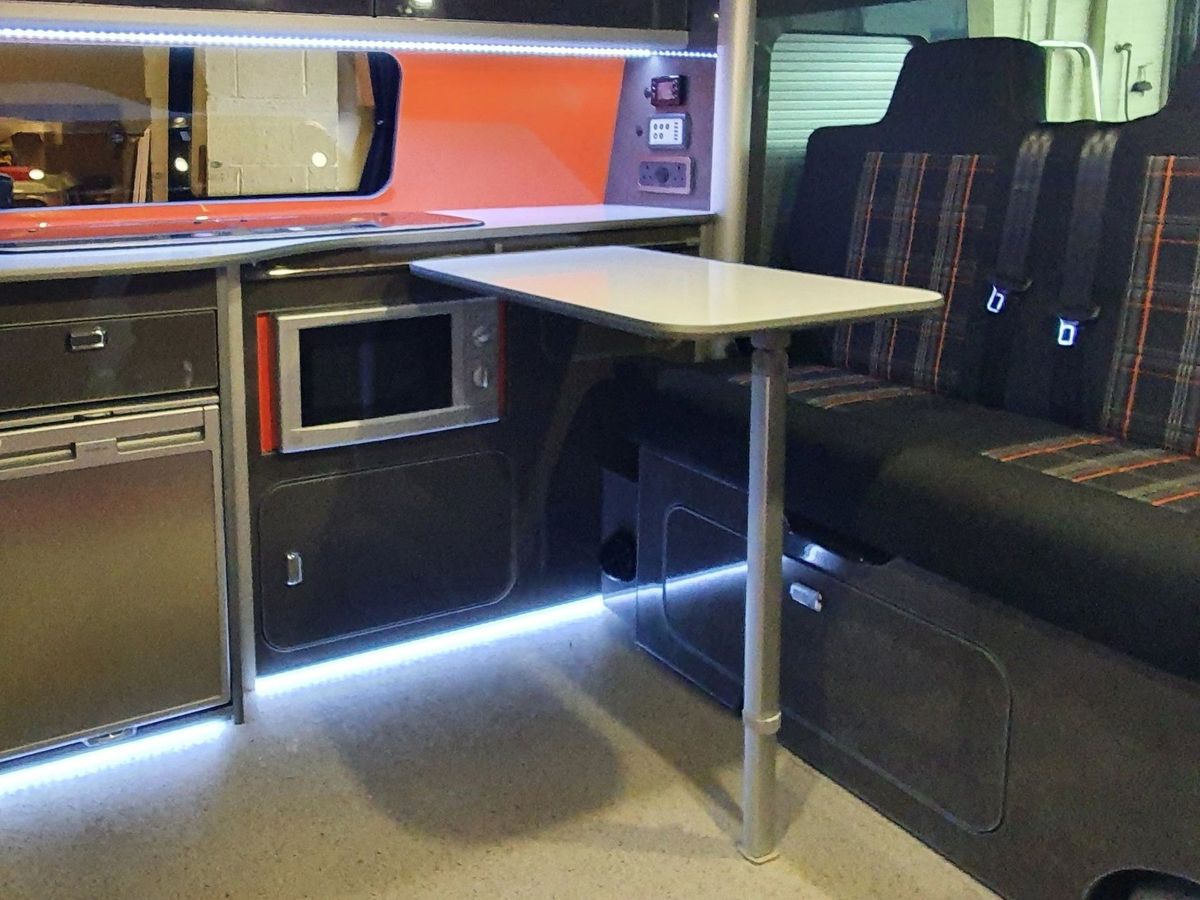 Kitchen with an orange splashback, a table and a tartan bench seat